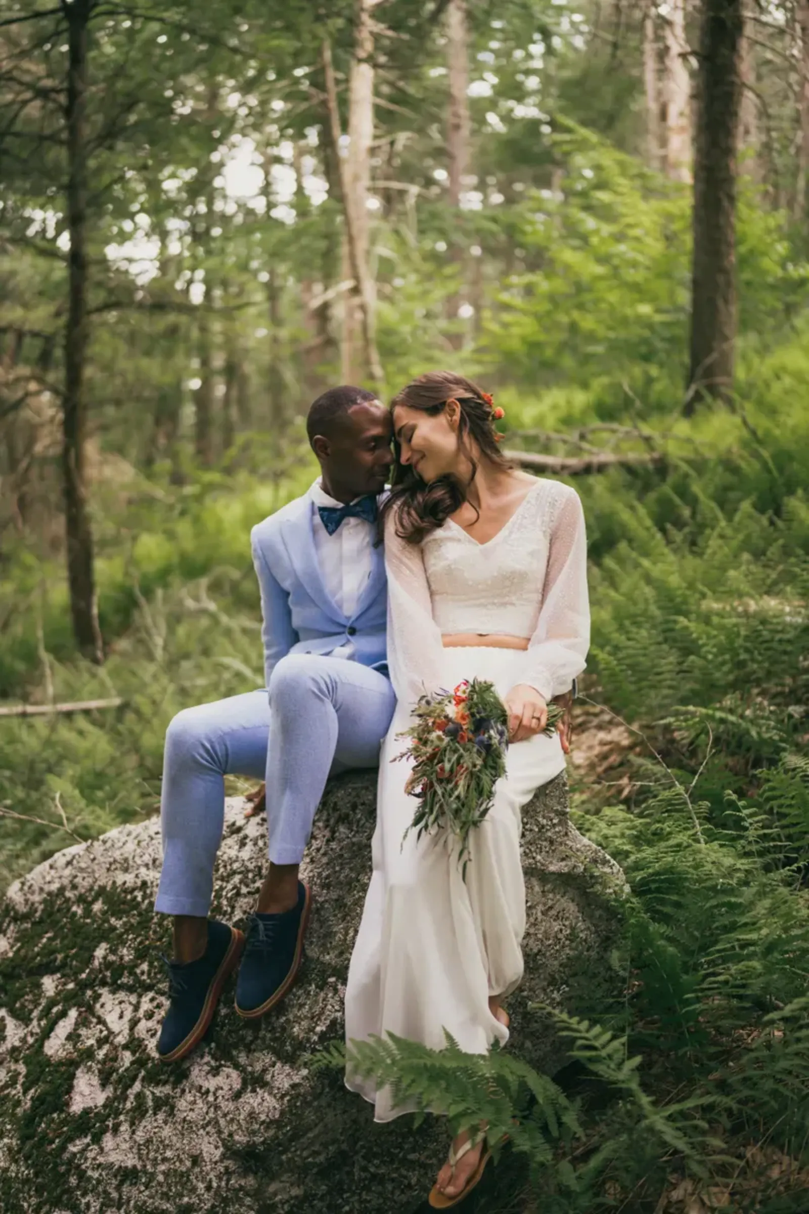Intimate Catskills elopement portrait of bride and groom sitting together among ferns in a lush forest