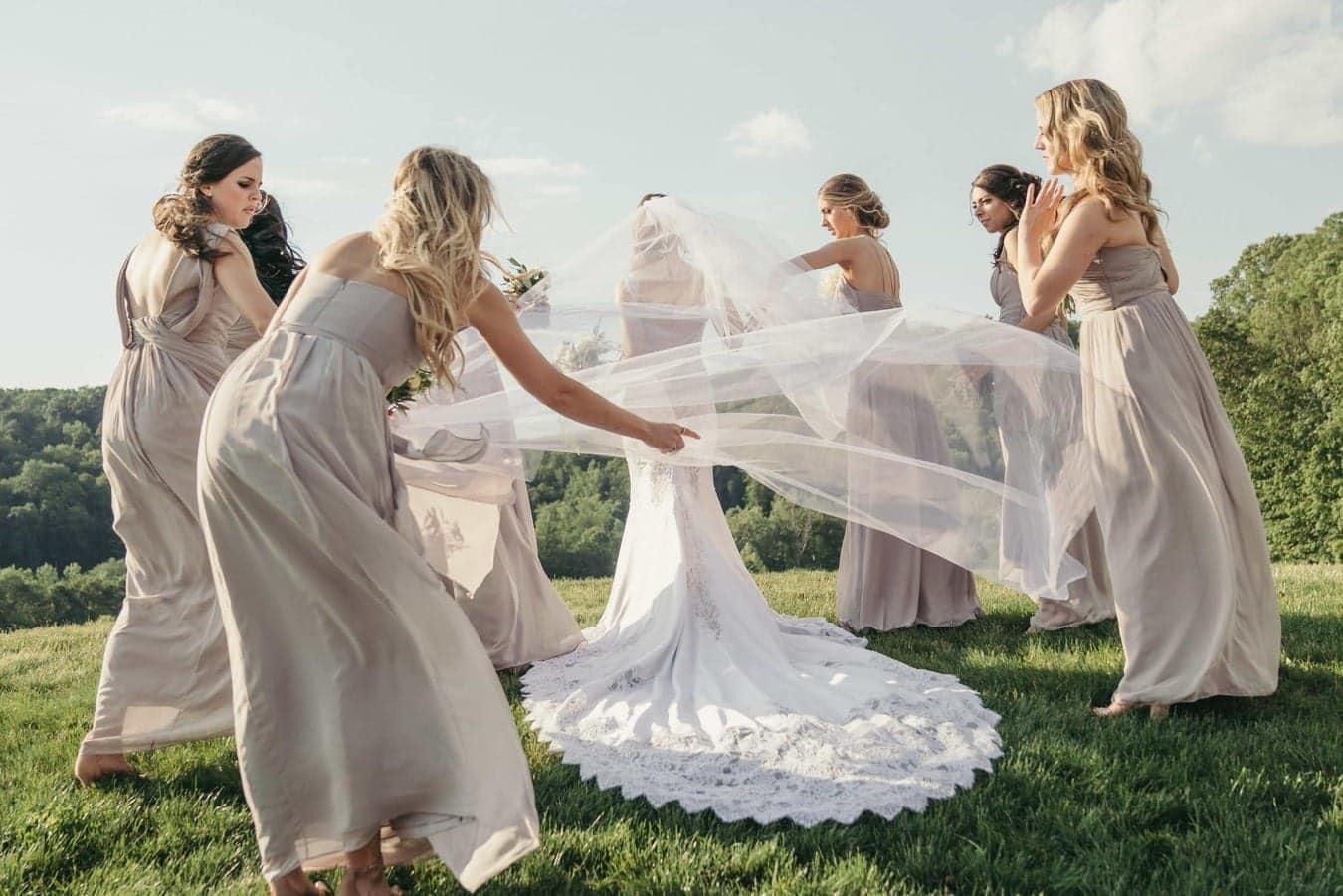 Bridesmaids circle around bride and one holds bride's veil as the wind blows it.