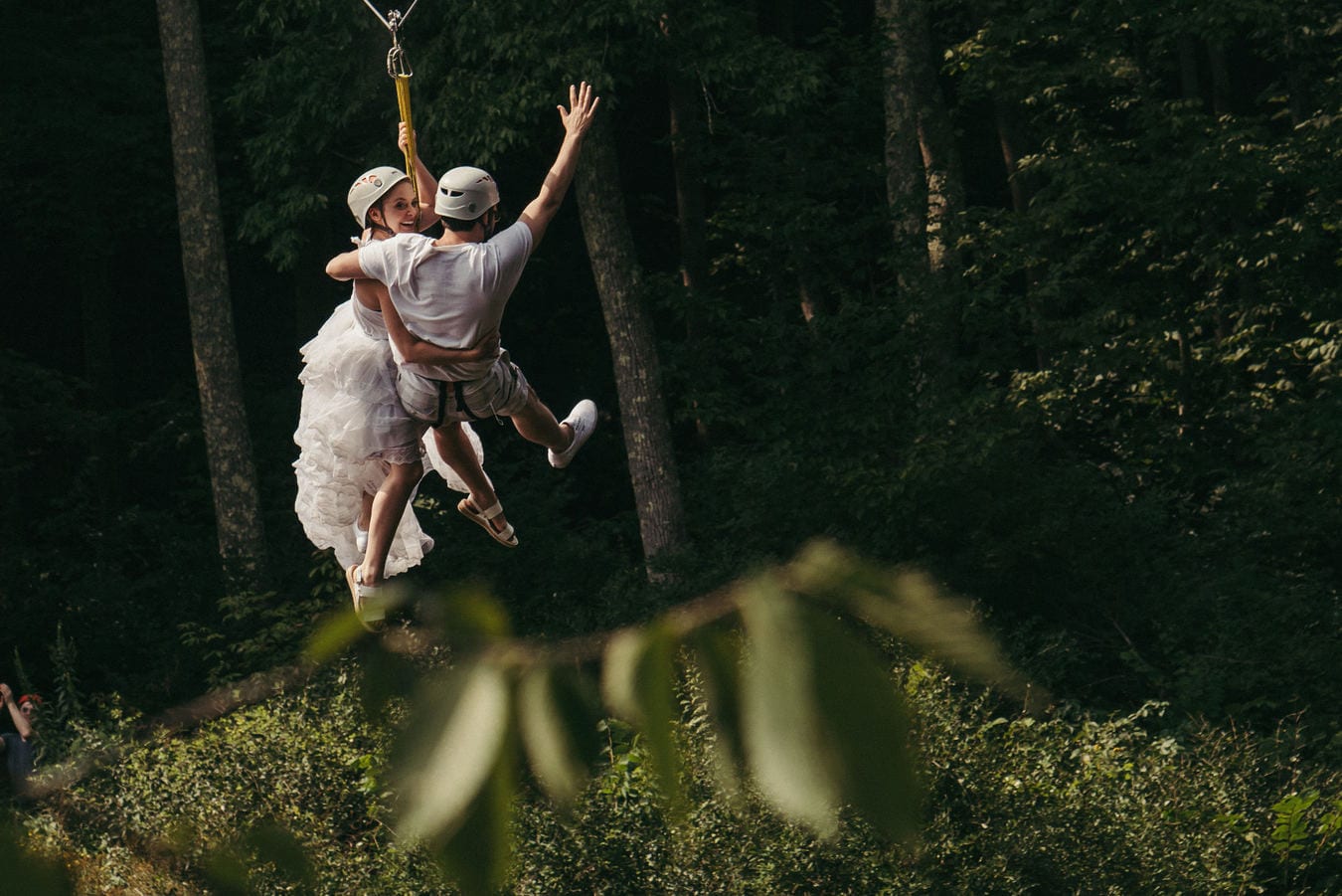 Bride and groom ride zip line through Catskill forest after wedding ceremony.