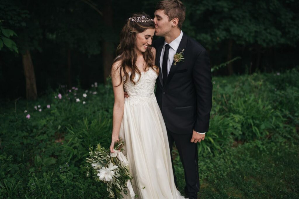 Groom kisses bride on the head while bride smiles at Hudson Valley wedding venue.