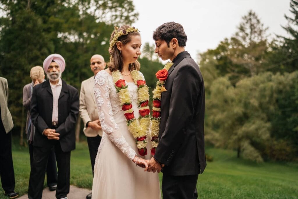 Bride and groom hold hands and stand together, eyes closed, before Indian wedding ceremony.