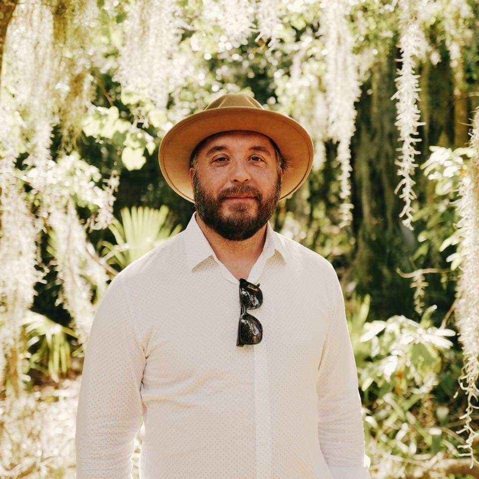 Joshua stands in front of hanging moss and tropical leaves.