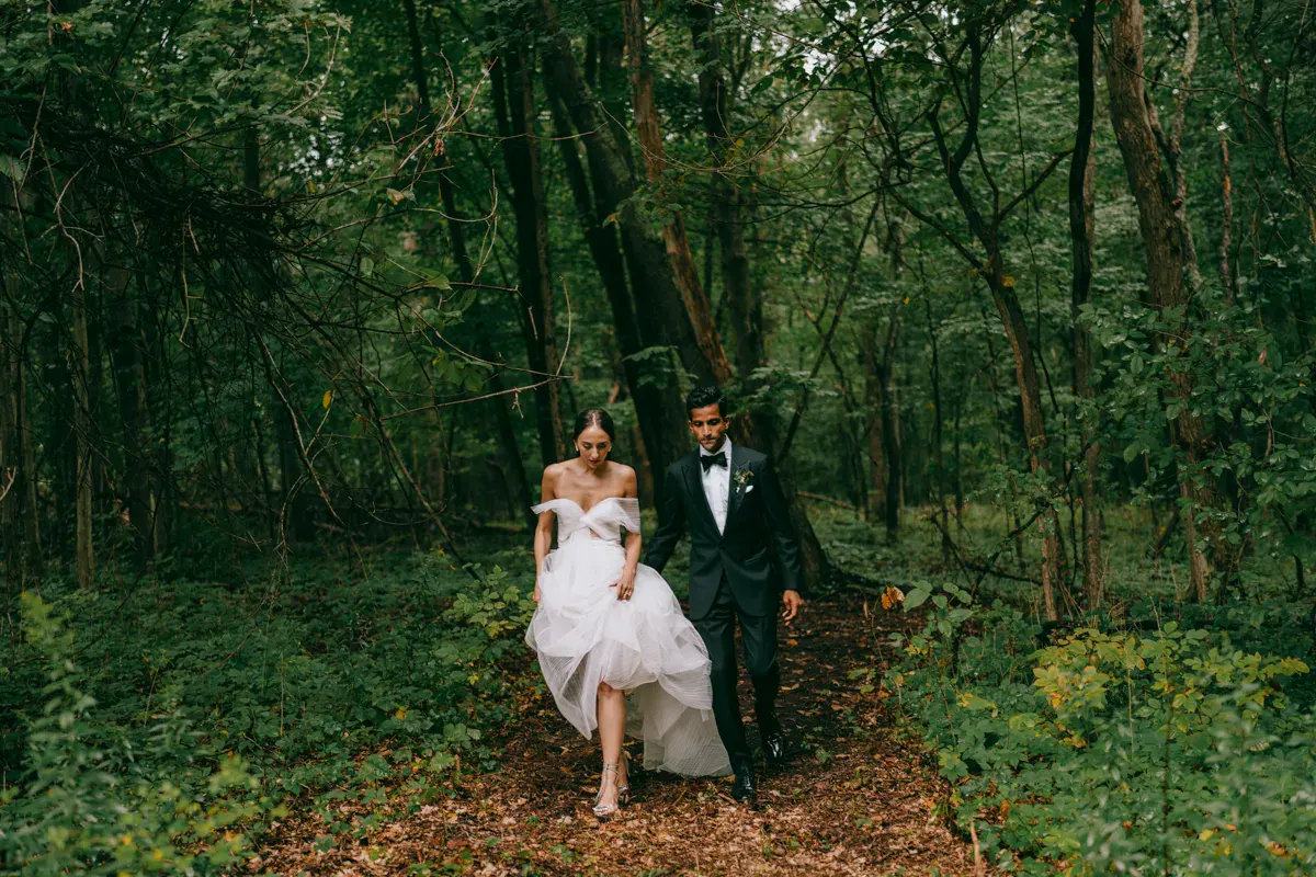Couple walking hand-in-hand through a lush green forest path during Old Mill wedding portraits, Hudson Valley
