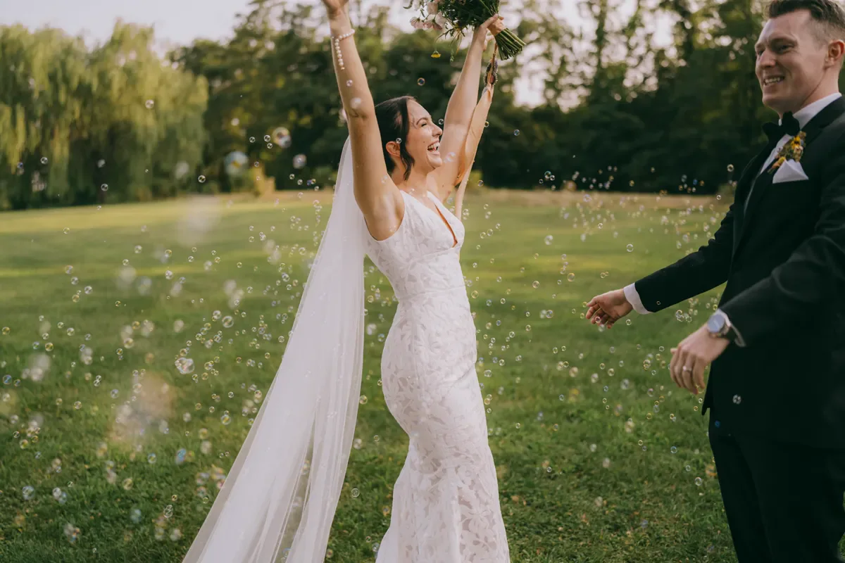 Bride in a flowing veil walking through a field with arms raised joyfully during wedding portraits, Hudson Valley