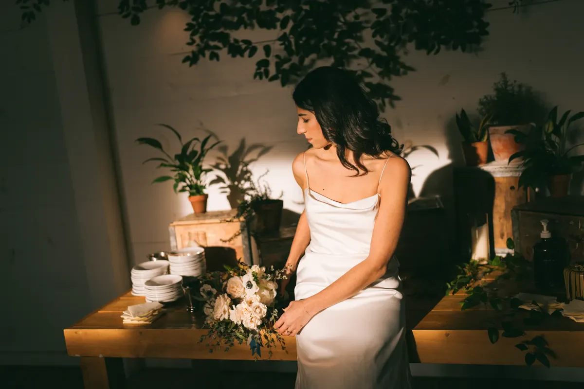 Bride in a strapless gown seated in a moody, candlelit corner with lush floral arrangements, Hudson Valley wedding