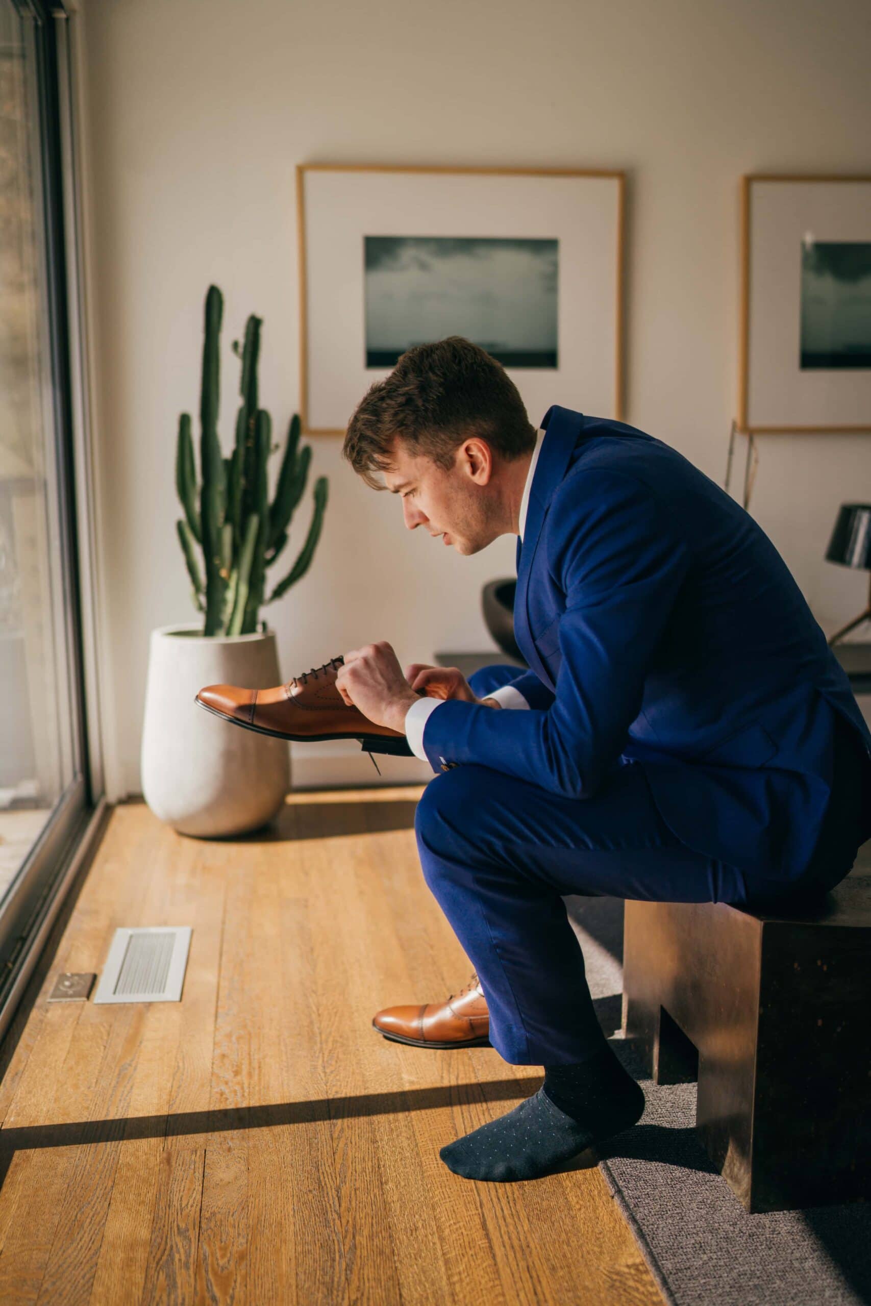 Groom puts shoes on before wedding ceremony inside midcentury home in Hudson Valley.