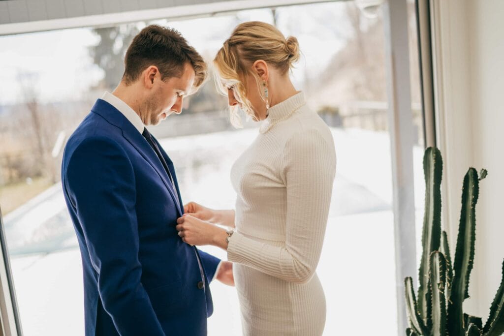 Bride buttons groom's jacket before wedding ceremony in Hudson Valley.