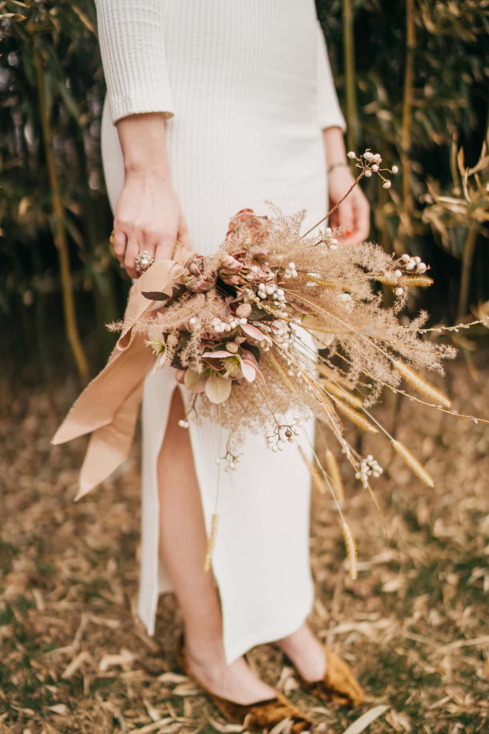 Bride holds dry brown grass and weeds bouquet.