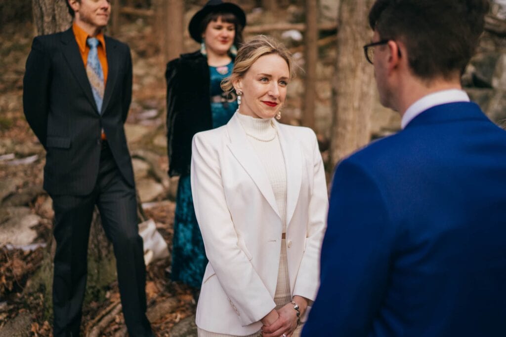 Bride smiles at groom during ceremony in Hudson Valley winter forest.