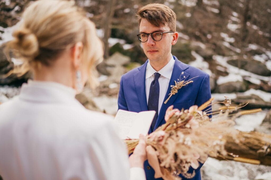 Bride reads groom vows during ceremony in Hudson Valley winter forest.