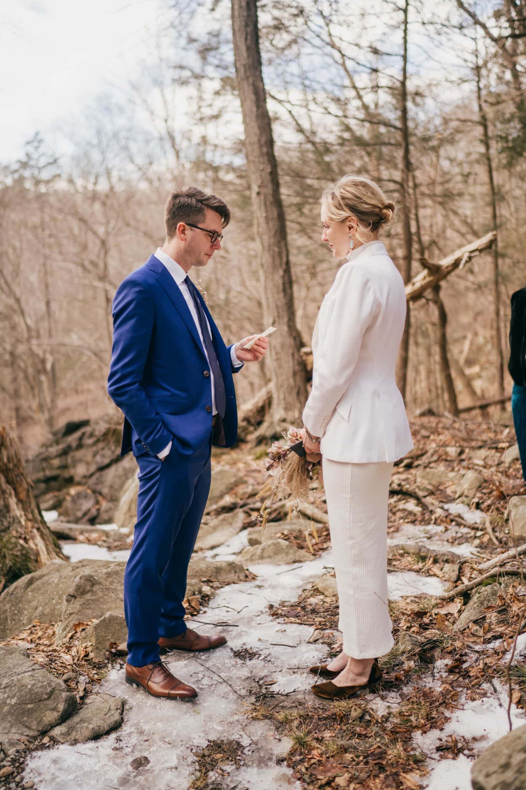 Groom reads bride vows during ceremony in Hudson Valley winter forest.