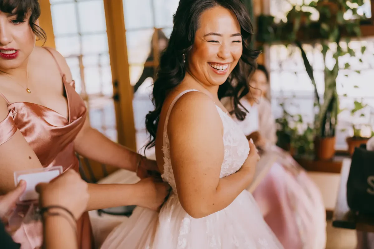Bridesmaid in a pink dress laughing candidly during wedding preparations at Blooming Hill Farm, Hudson Valley