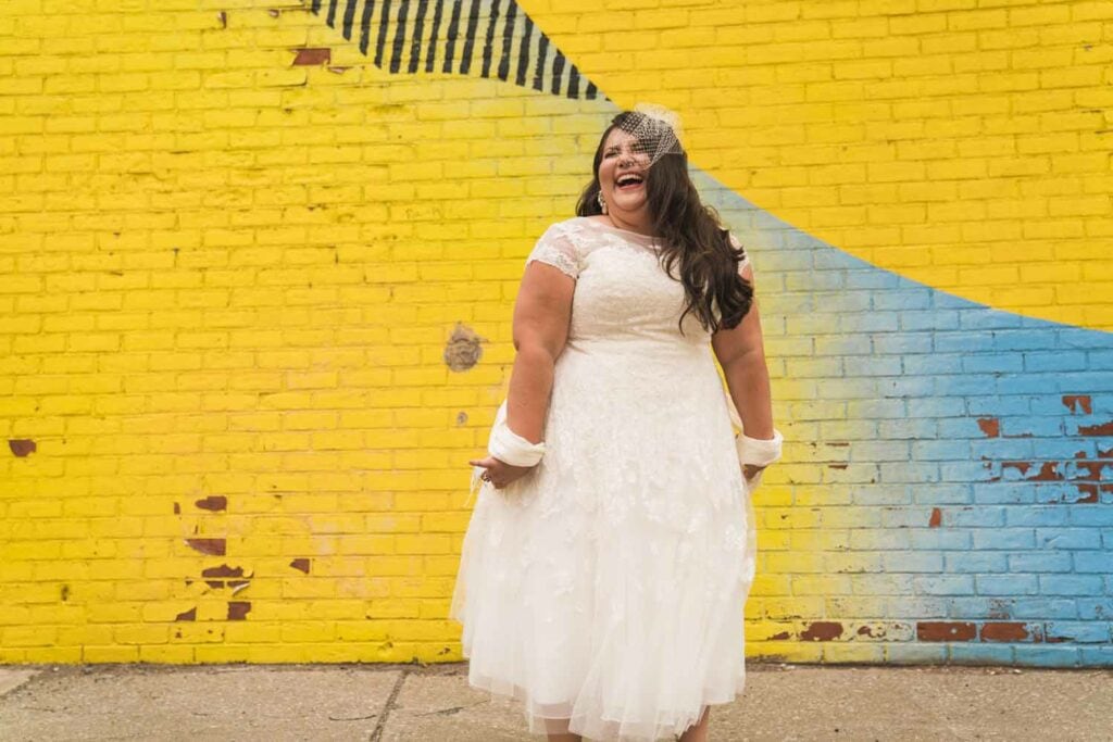 Joyful bride laughing against yellow wall.