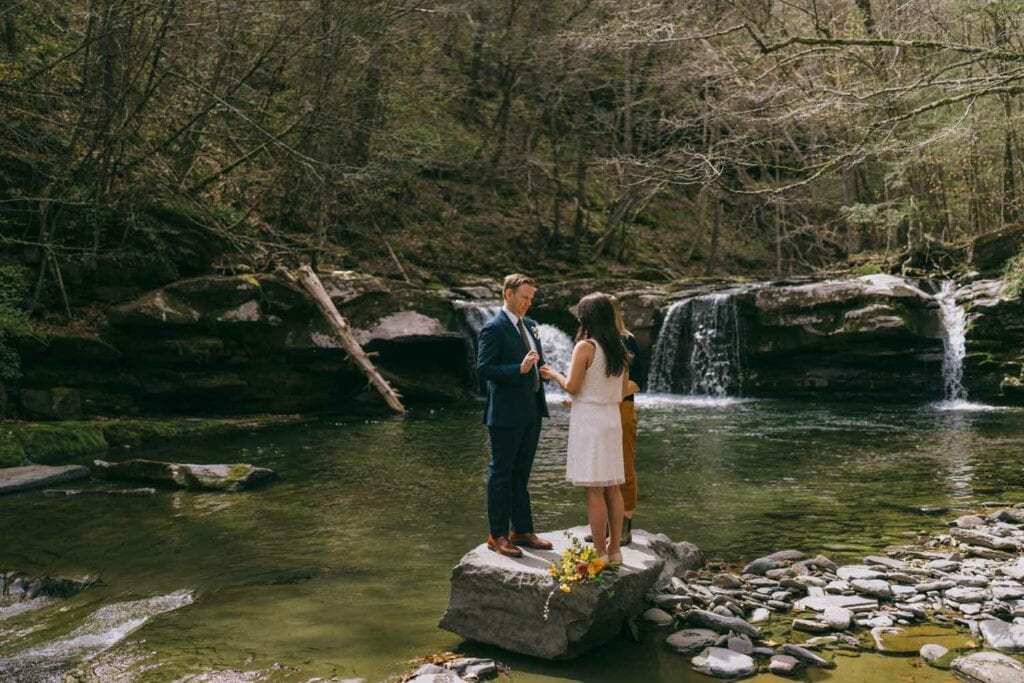 Couple holding hands by forest waterfall.