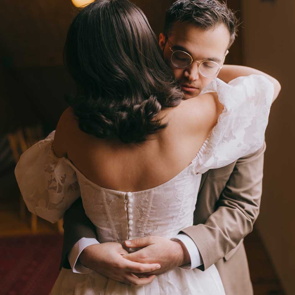 Bride and groom embrace, bathed in natural window light.