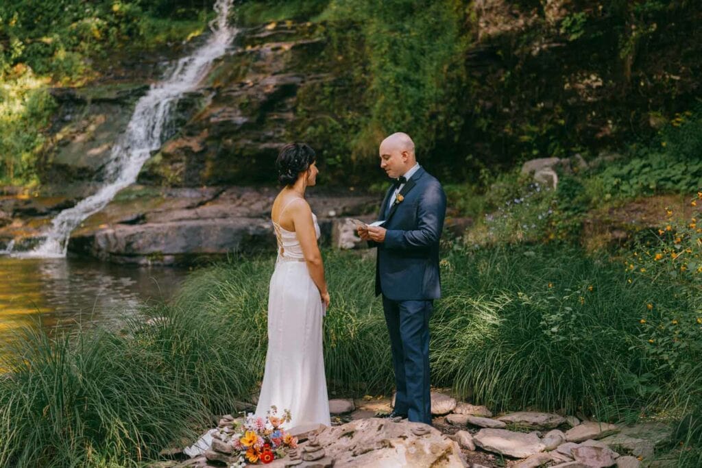 Couple exchanging vows by waterfall outdoors.