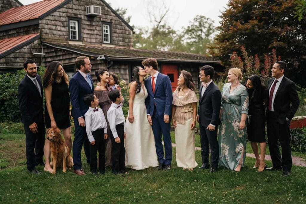 Bridal couple kissing, family and dog, outdoor wedding.