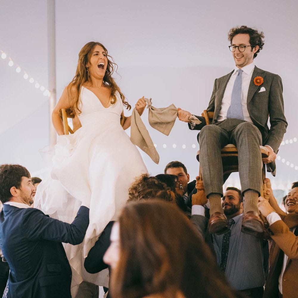 Bride and groom lifted in chairs at during the hora at their wedding reception.