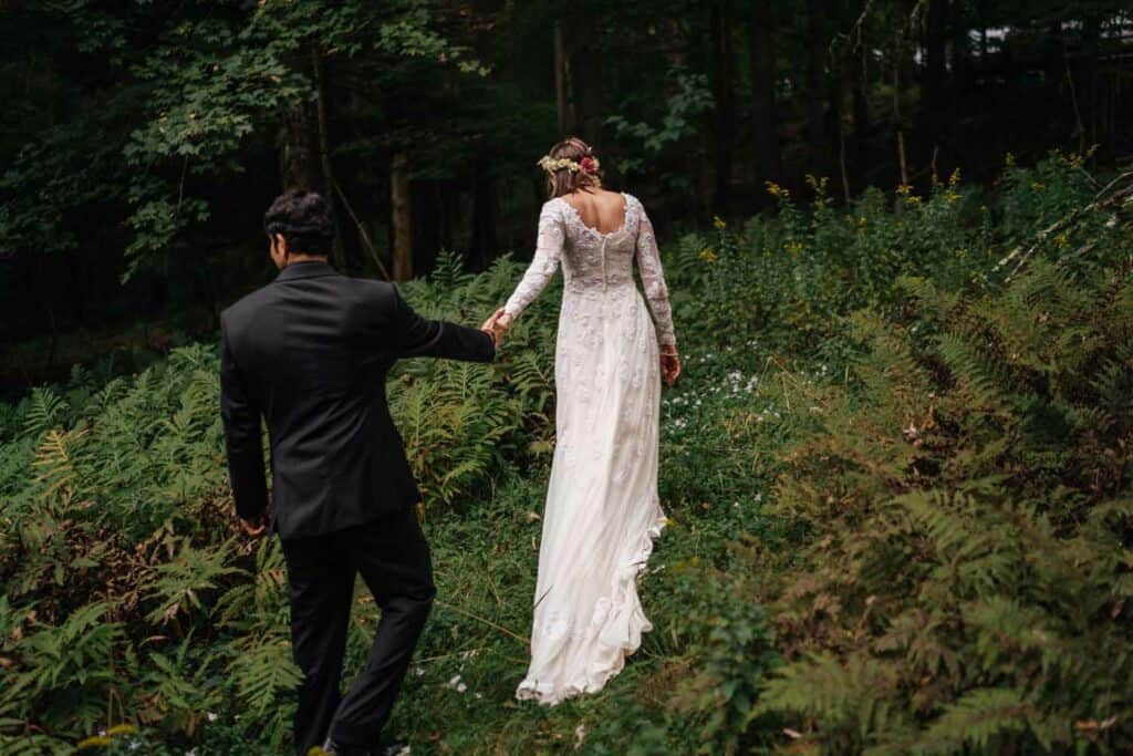 Bride and groom walking in forest clearing.