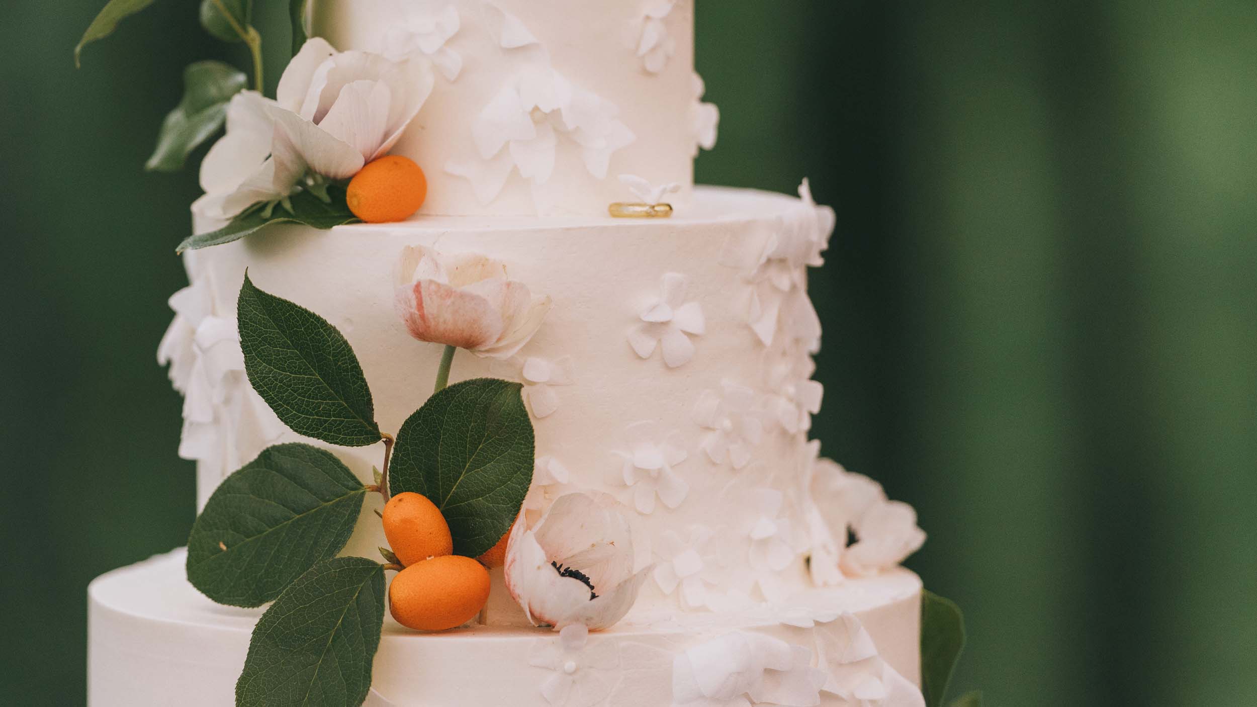 A three-tiered white wedding cake is decorated with anemones and kumquats still on the branch. 