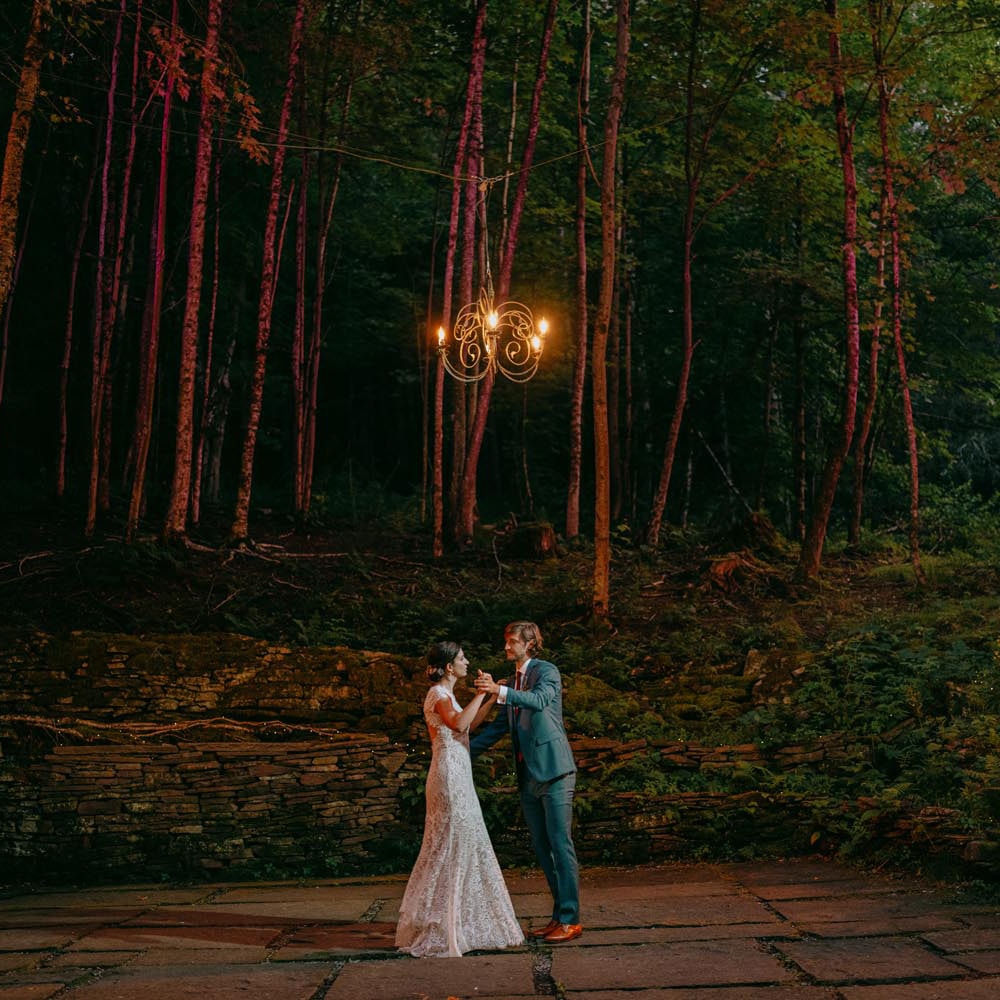 Couple dancing under lights in forest wedding setting.